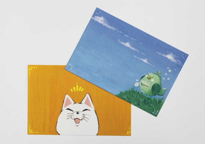 絵葉書２枚の写真。黄色い背景に猫が描かれたイラストと、空色の背景に鳥が描かれたイラストが印刷されています。